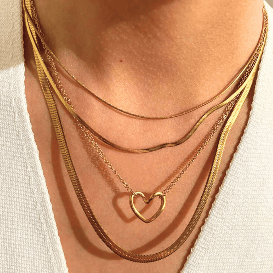 Gold necklaces with a heart-shaped pendant on a person wearing a white top.