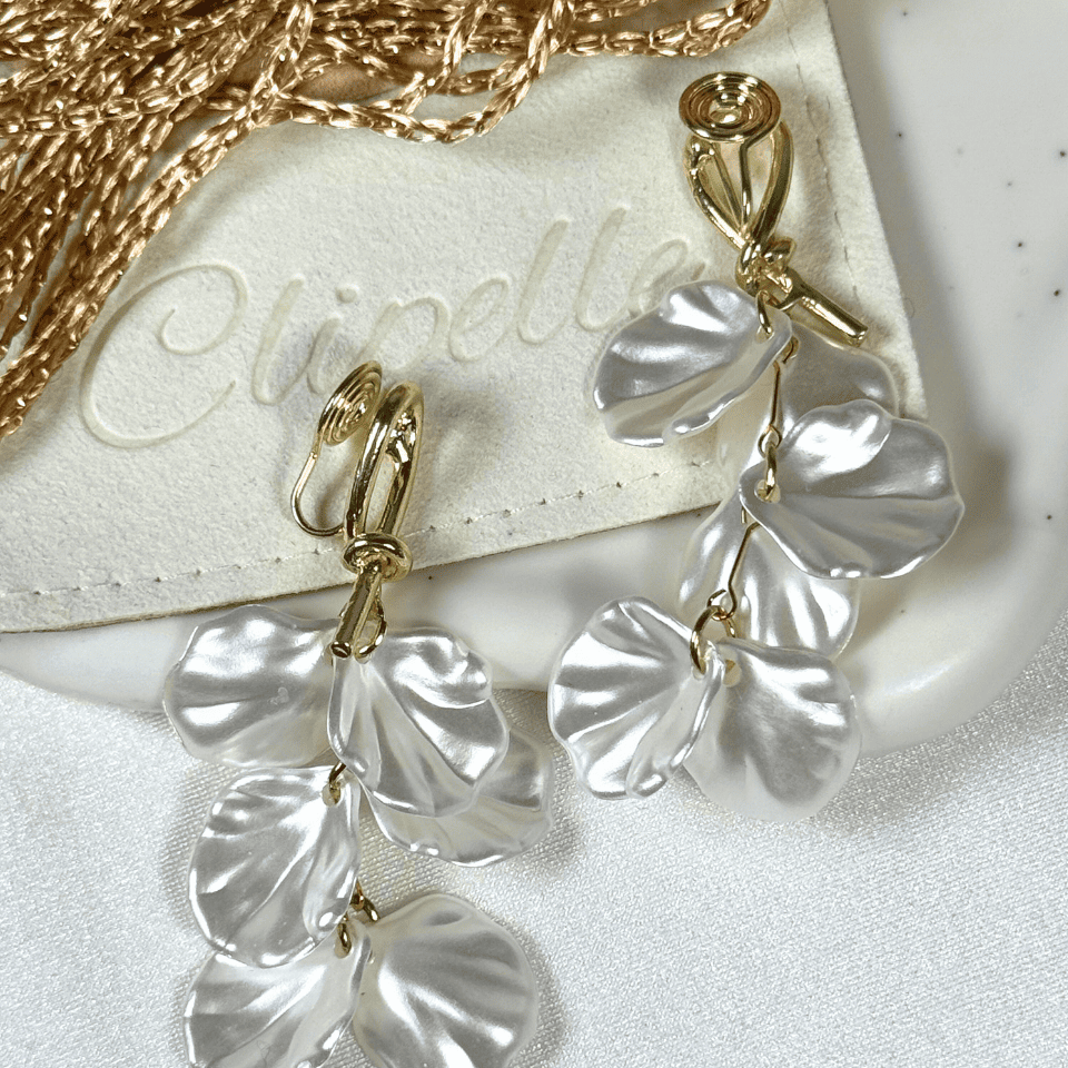 Gold and white floral earrings on a white surface with 'Clinelle' branding.