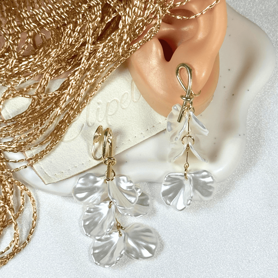 Gold and white earrings worn on an ear with gold chains in the background