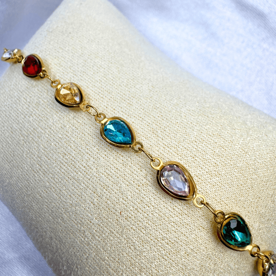 Gold bracelet with multicolored gemstones on a white cushion
