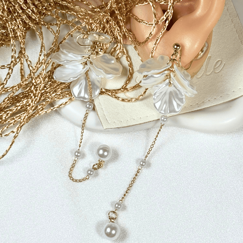 Gold earring with floral design and pearl chain on a white surface