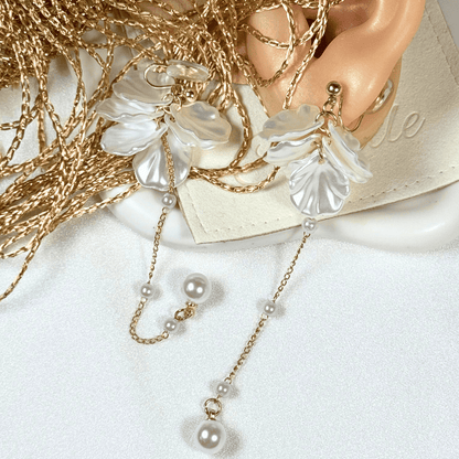 Gold earring with floral design and pearl chain on a white surface