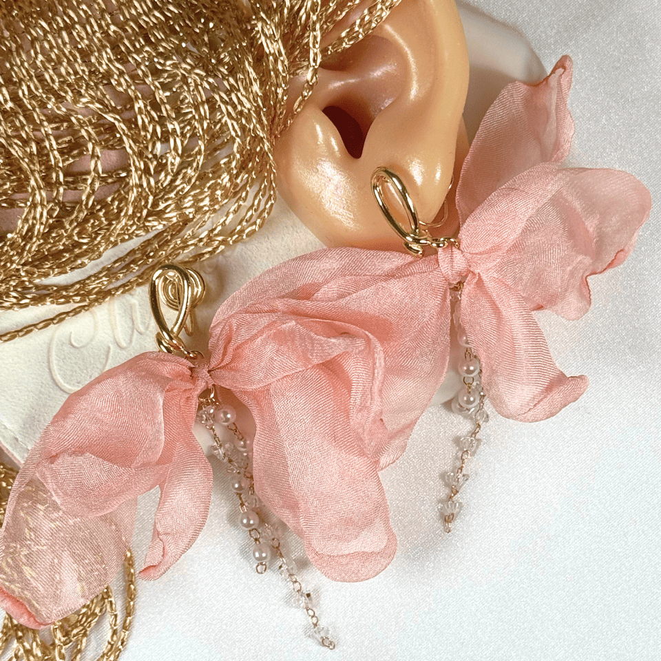 Gold earring with pink ribbon and pearl chain on a white background