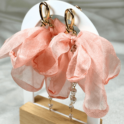 Pink floral earrings with gold accents on a white stand.