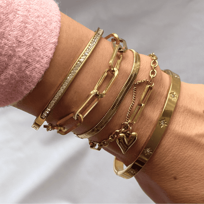 Gold bracelets on a wrist with a pink sleeve against a light background