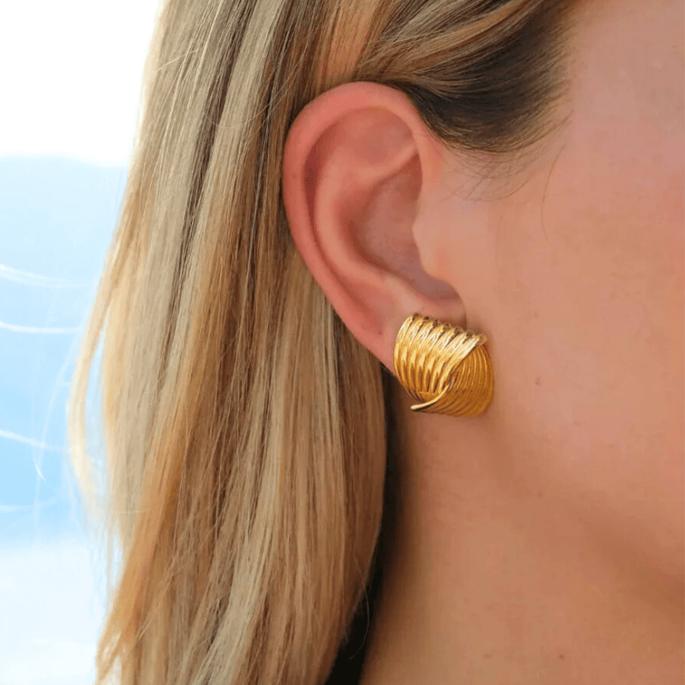 Gold hoop earrings worn by a person with blonde hair against a blue sky.