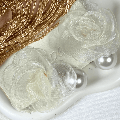 Decorative ribbon with sheer white roses and pearl accents on a white surface.