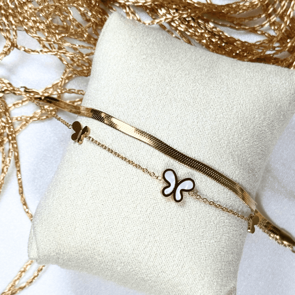 Gold bracelet with butterfly charm on a white cushion