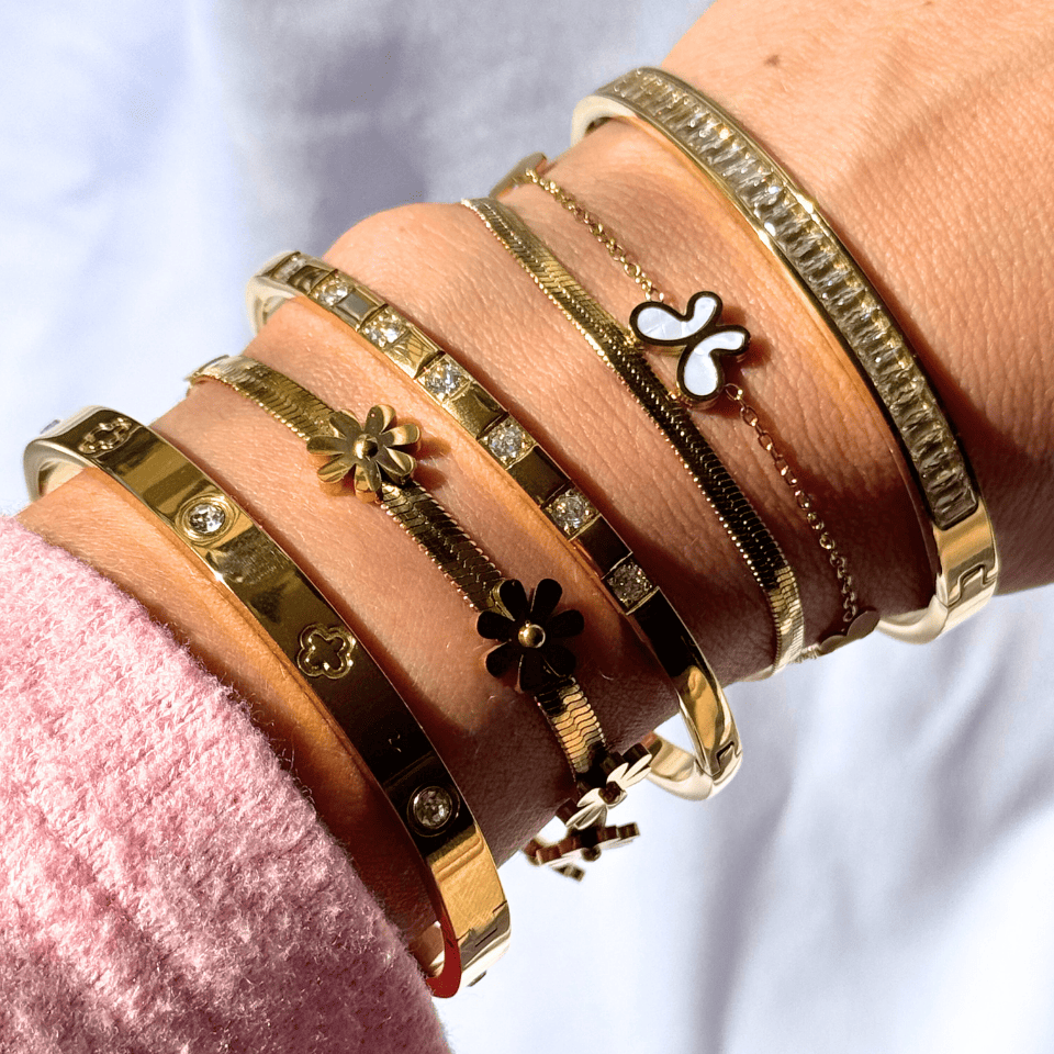 Close-up of a wrist wearing multiple gold bracelets with various designs on a blurred background.