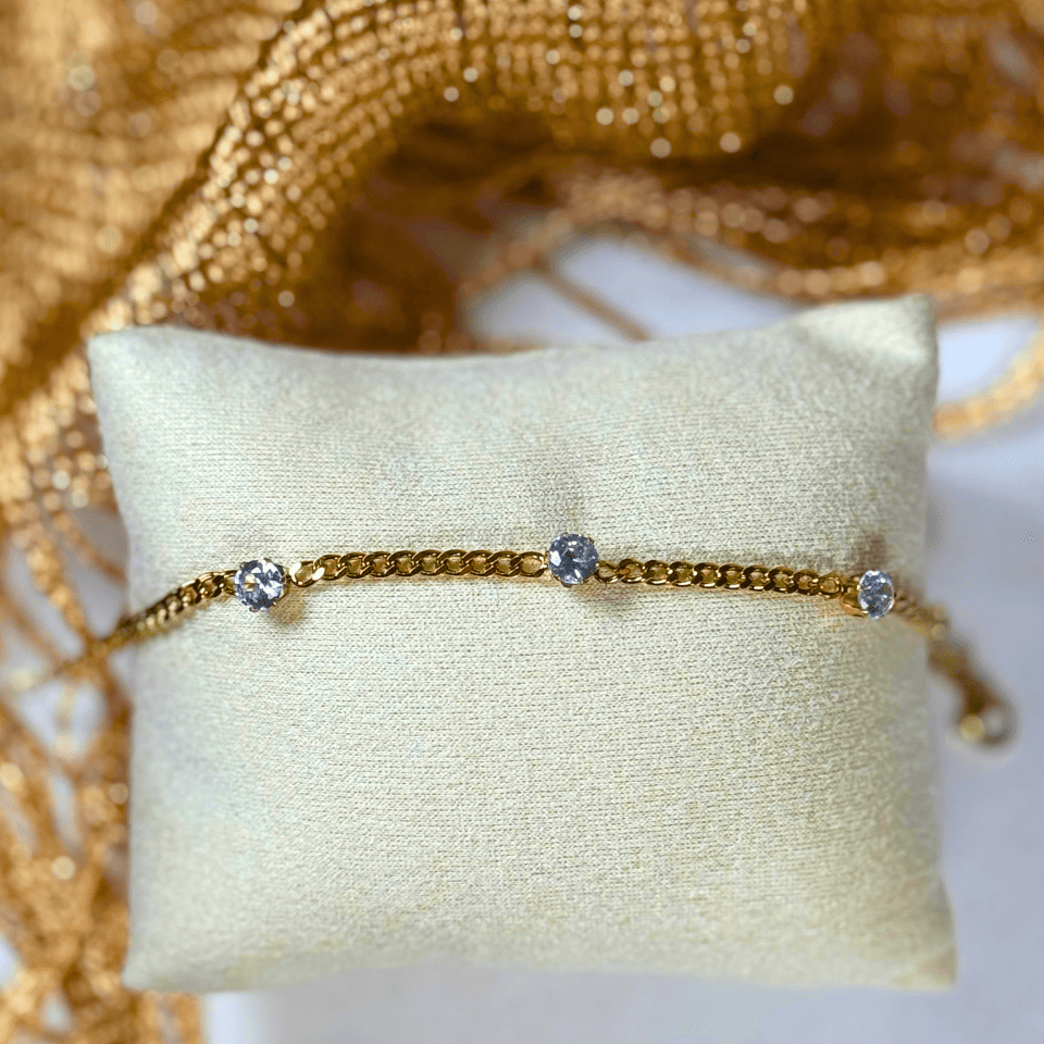 Gold bracelet with small crystals on a beige pillow with a gold fabric background