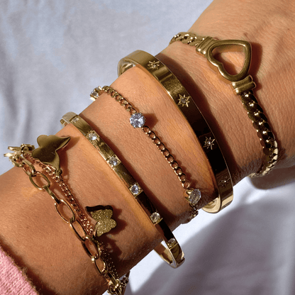 Close-up of a wrist wearing multiple gold bracelets with various designs on a light background.