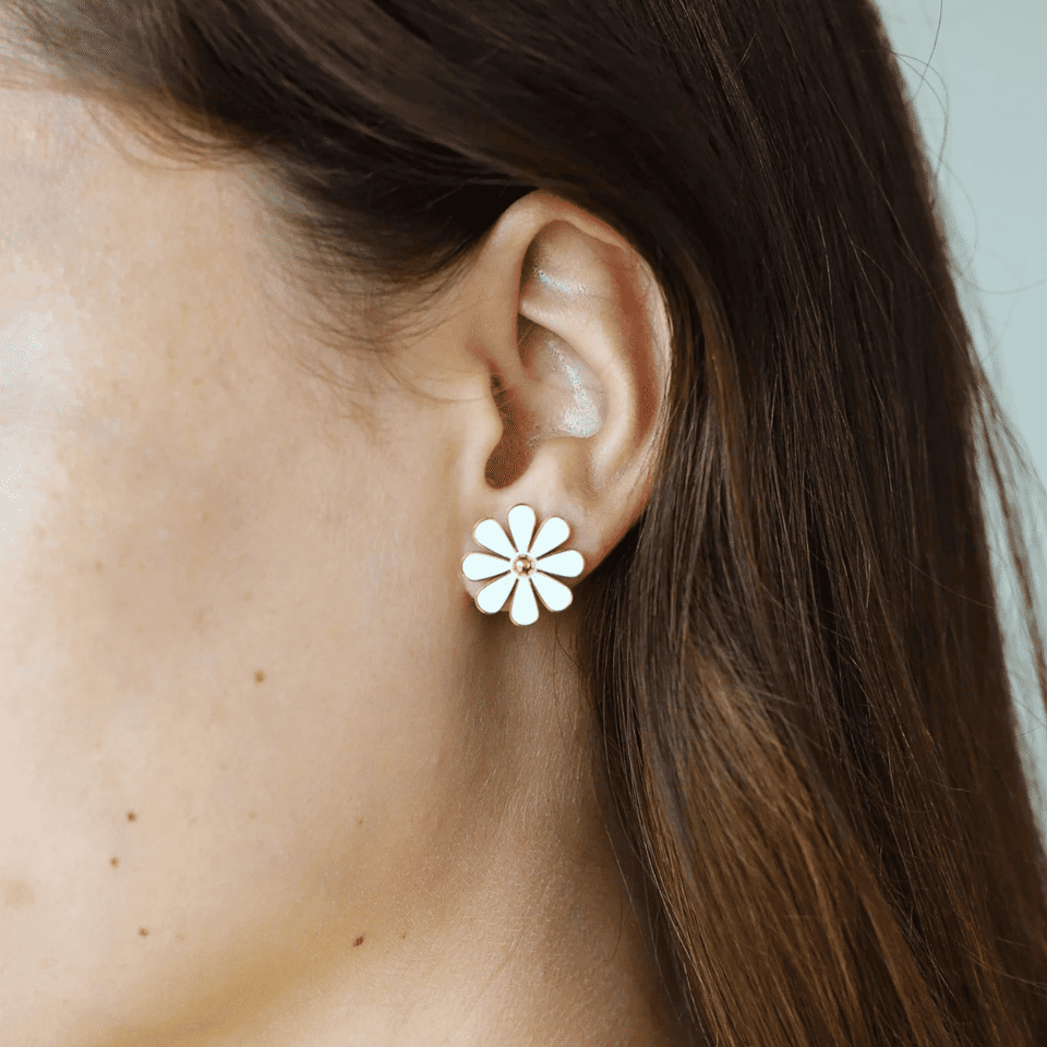 Close-up of an ear wearing a white flower-shaped earring with a blurred background