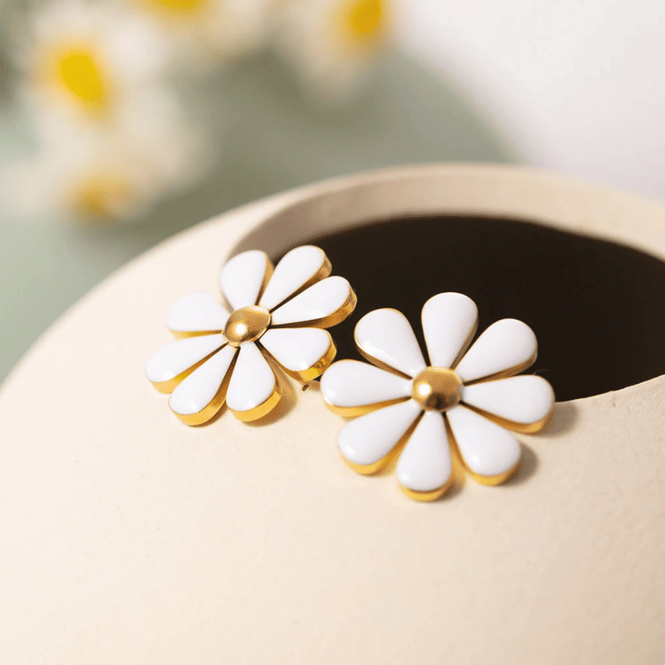 White flower-shaped earrings with gold accents on a beige surface.