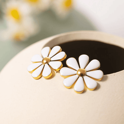 White flower-shaped earrings with gold accents on a beige surface.