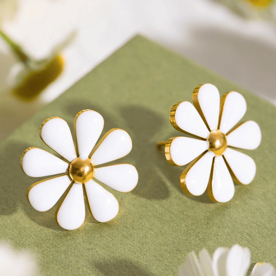 White flower-shaped earrings with gold centers on a green surface
