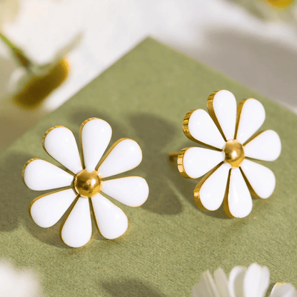 White flower-shaped earrings with gold centers on a green surface