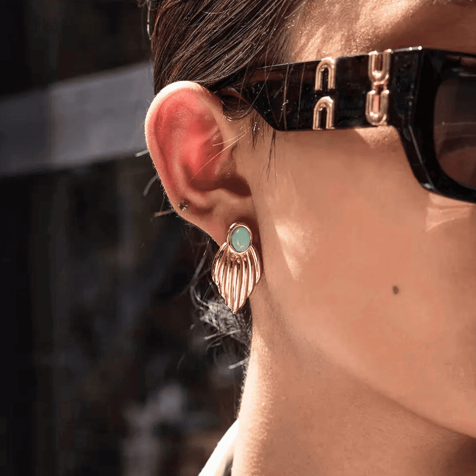 Close-up of an ear wearing a gold earring with a turquoise stone, with sunglasses on the head.