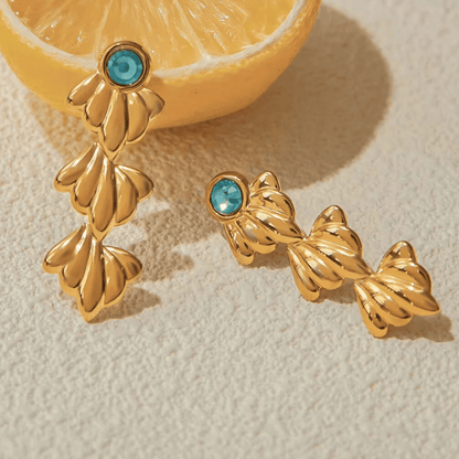 Gold earrings with turquoise stones on a textured surface with a lemon slice.