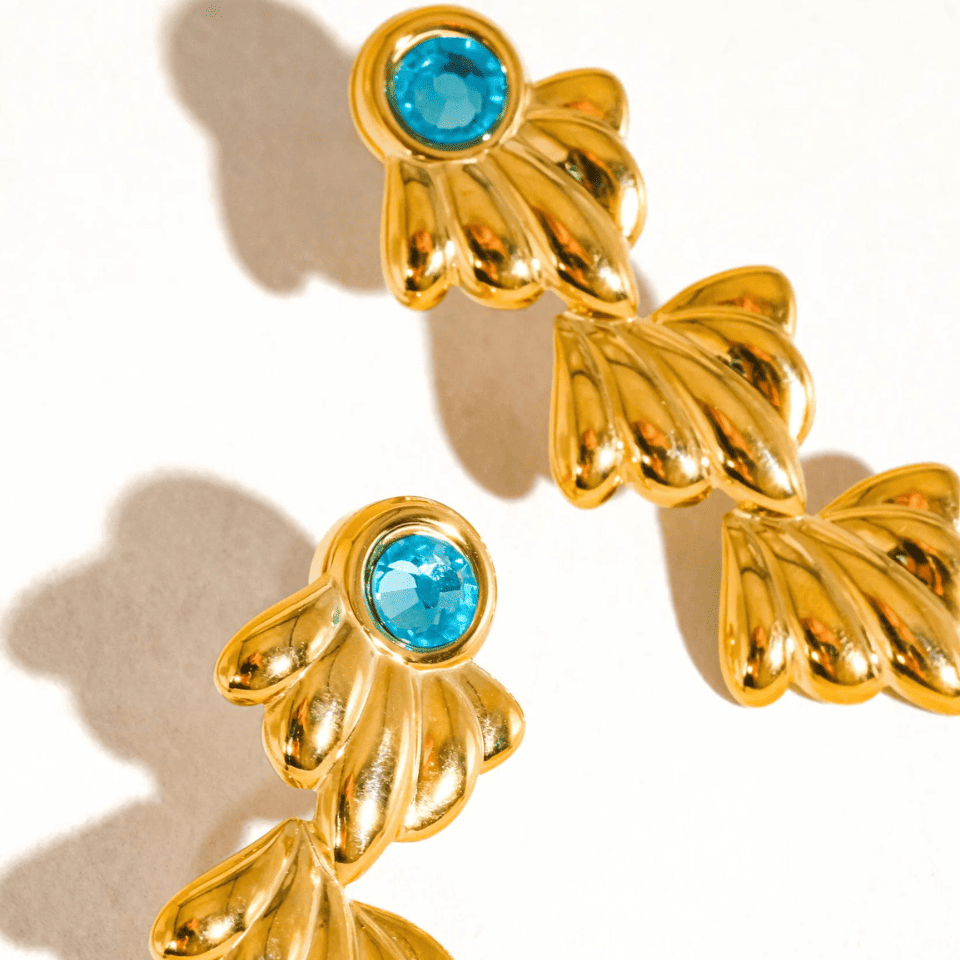 Gold earrings with blue gemstones on a beige background