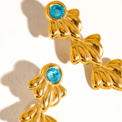 Gold earrings with blue gemstones on a beige background