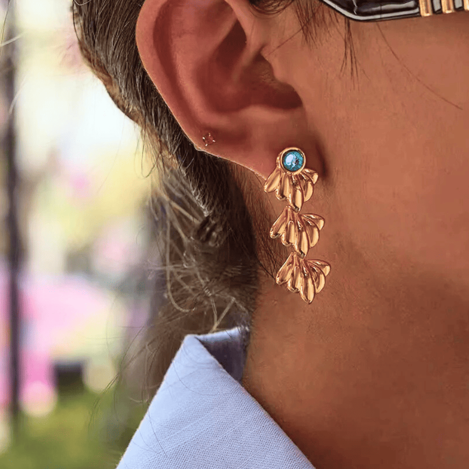 Close-up of a person wearing gold earrings with a blurred outdoor background