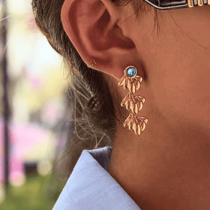 Close-up of a person wearing gold earrings with a blurred outdoor background