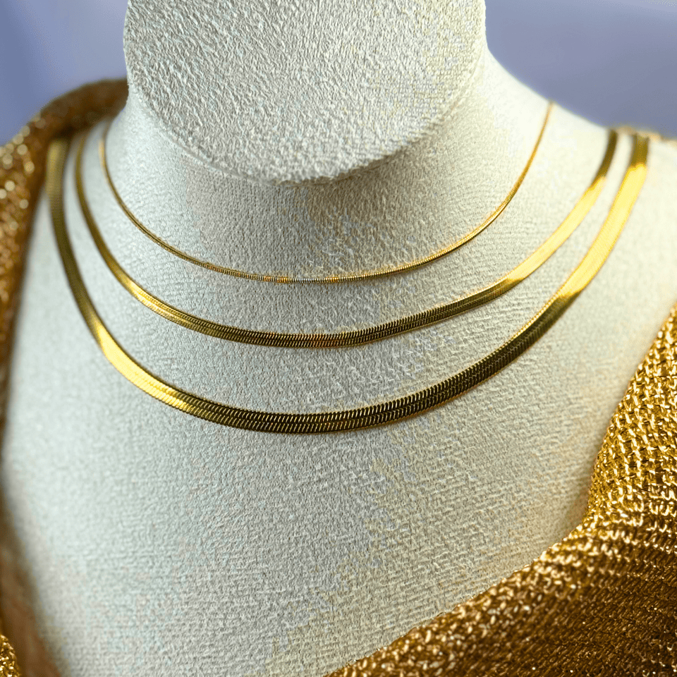 Three gold necklaces on a mannequin bust with a gold background