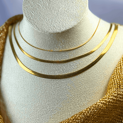 Three gold necklaces on a mannequin bust with a gold background