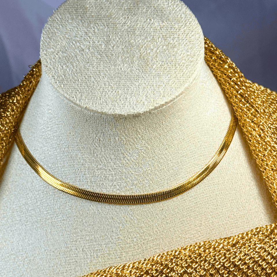 Gold necklace on a mannequin bust with a textured gold garment.