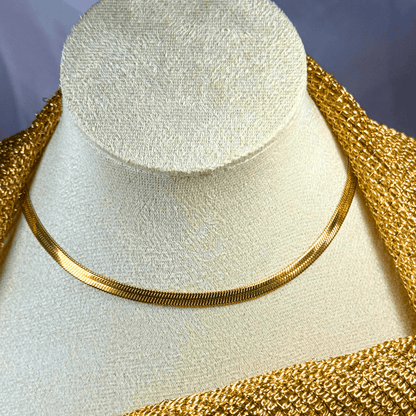 Gold necklace on a mannequin bust with a textured gold garment.