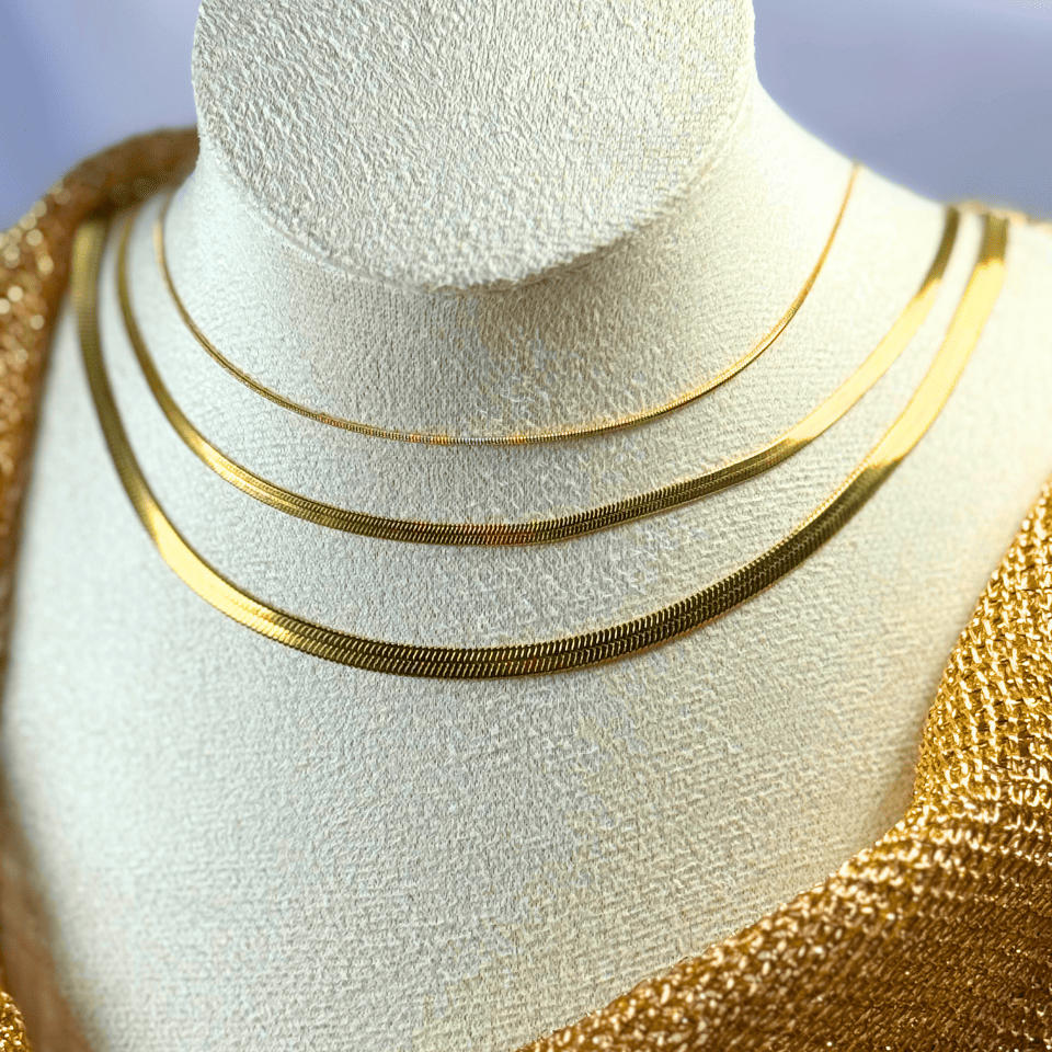 Gold necklaces on a mannequin bust with a neutral background