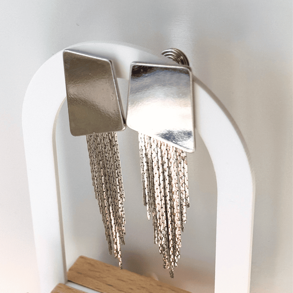 Silver fringe earrings on a white stand with a neutral background