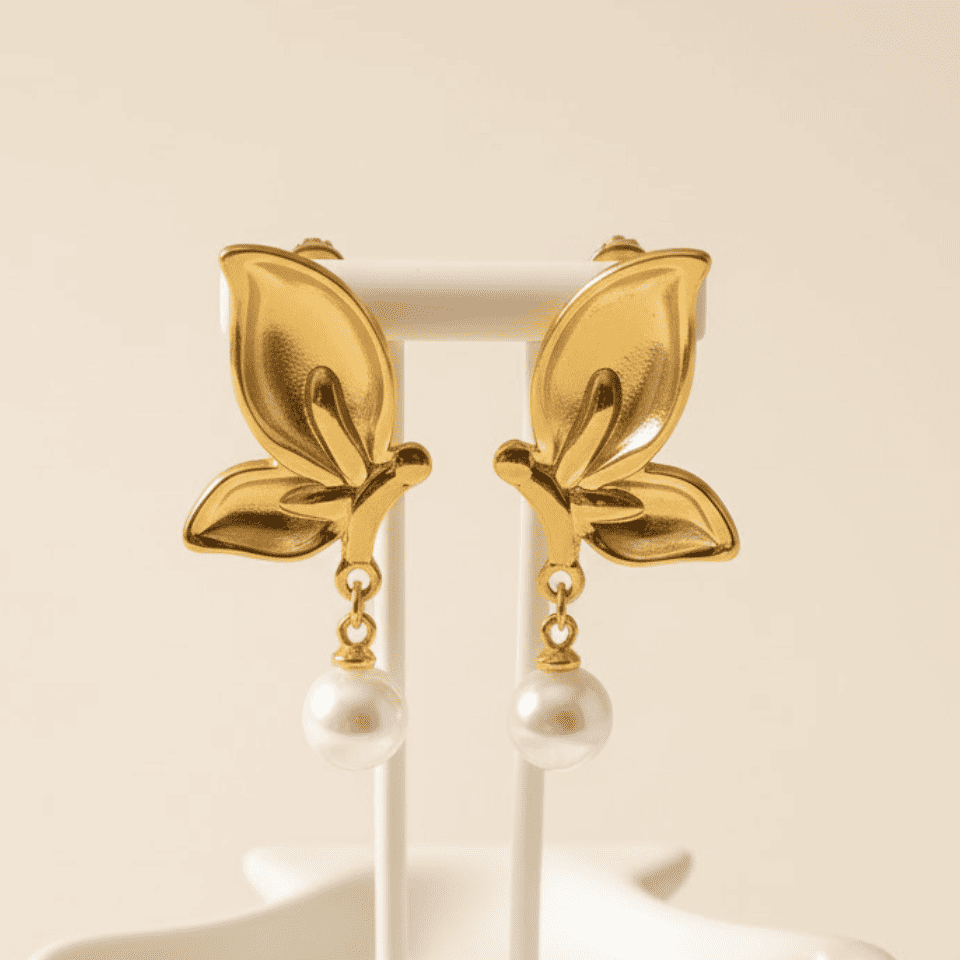 Gold leaf earrings with pearl drops on a white stand against a beige background