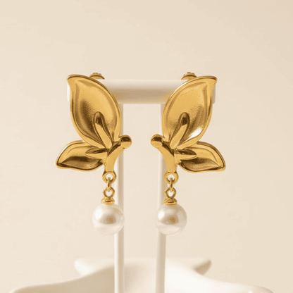 Gold leaf earrings with pearl drops on a white stand against a beige background