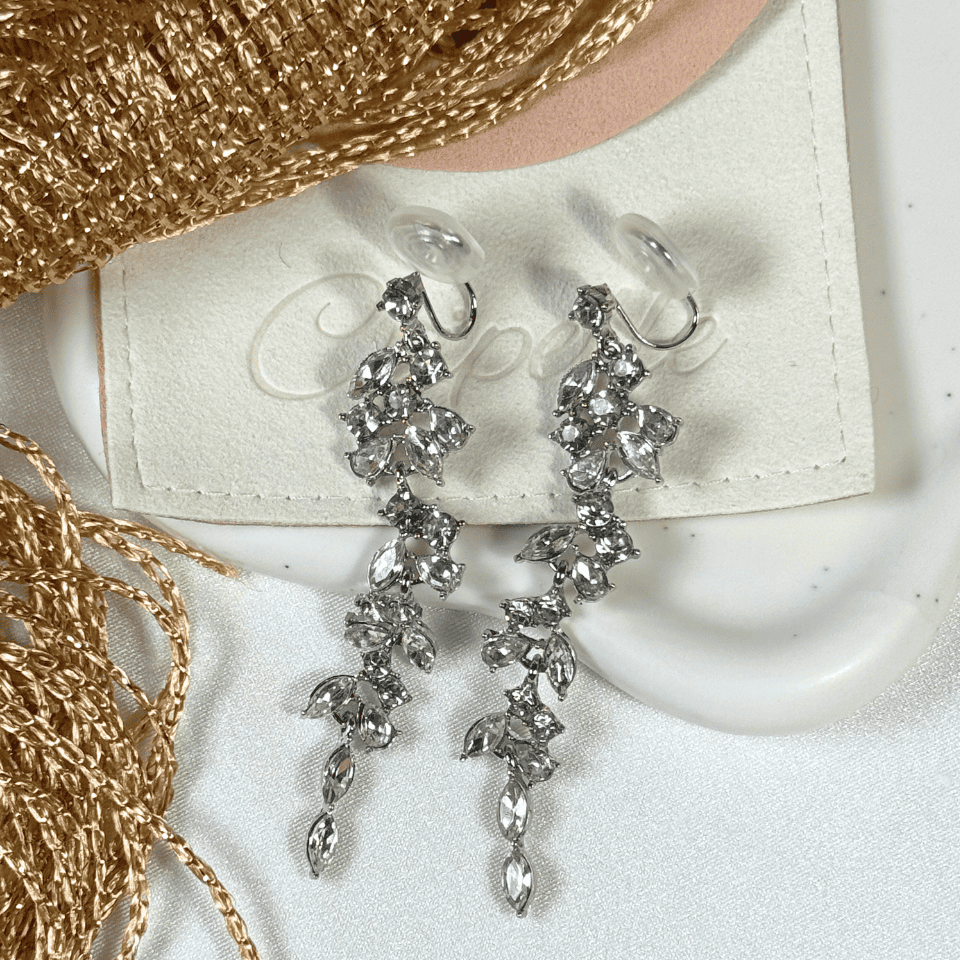 Silver earrings on a white stand with gold chain and fabric in the background