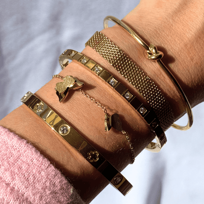 Close-up of a wrist wearing multiple gold bracelets with various designs on a light background.