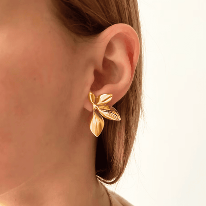Gold leaf earring worn by a person with a neutral background