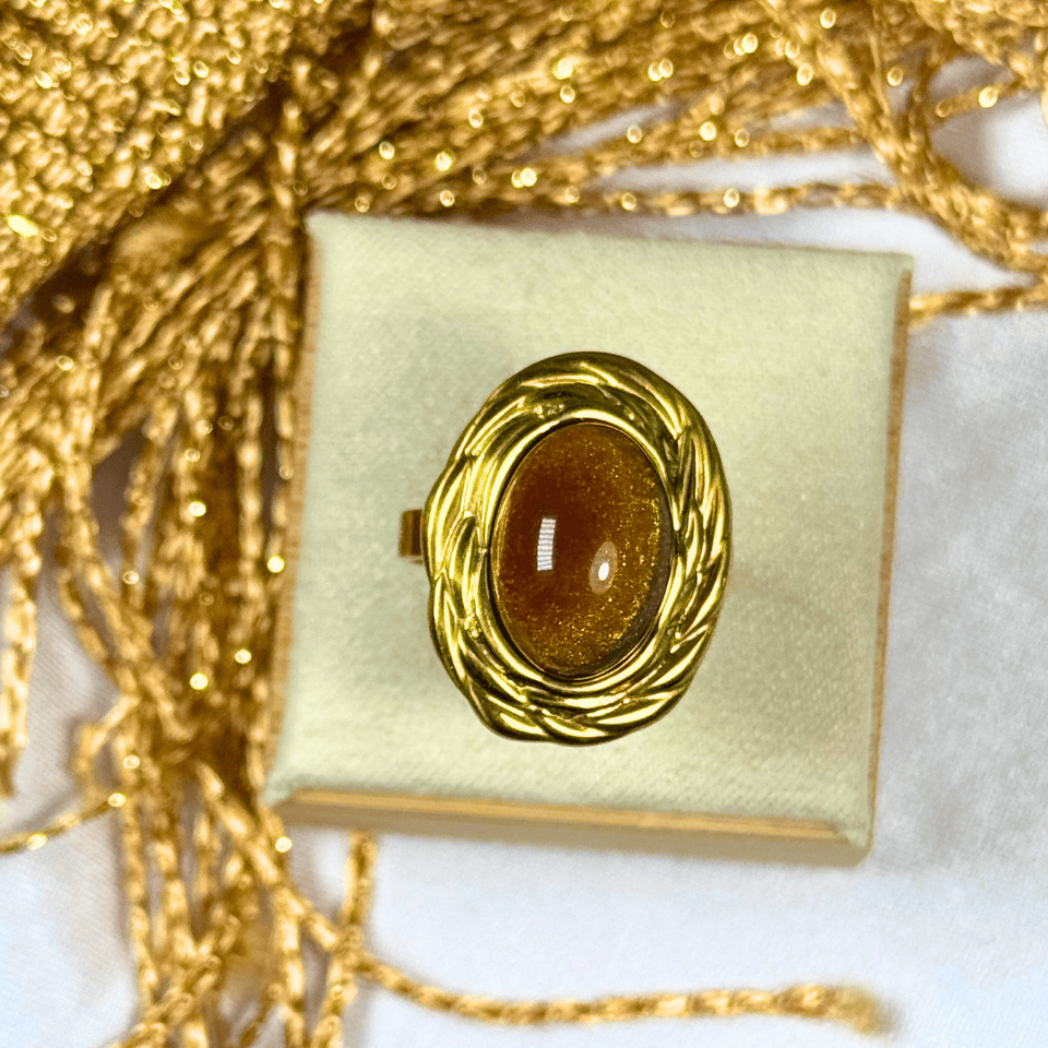 Gold ring with a brown gemstone on a gold box with a gold chain