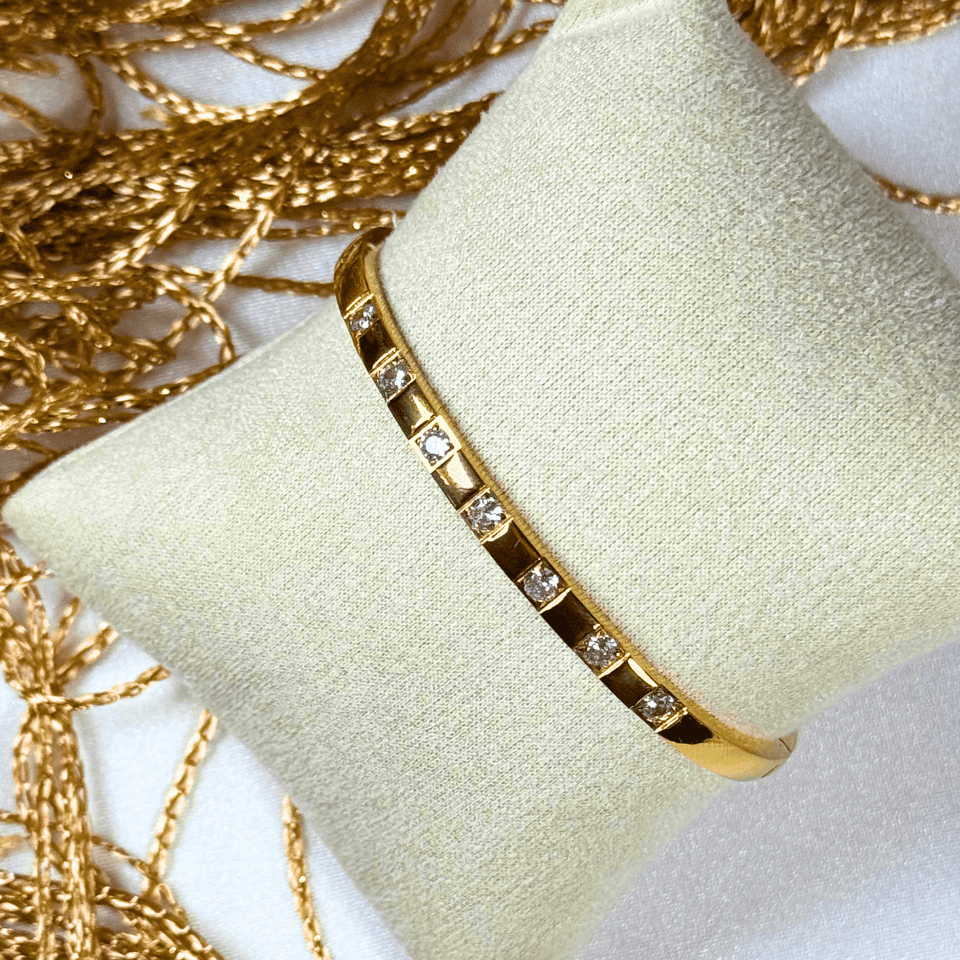 Gold bracelet with embedded stones on a light green cushion, surrounded by gold chains.