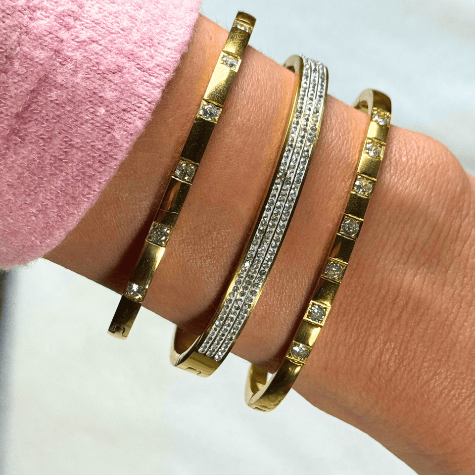 Gold and silver bracelets on a wrist with a pink fabric background