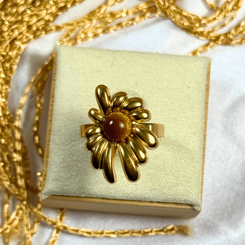Gold flower-shaped ring on a light green jewelry box with gold chain in the background