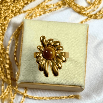 Gold flower-shaped ring on a light green jewelry box with gold chain in the background