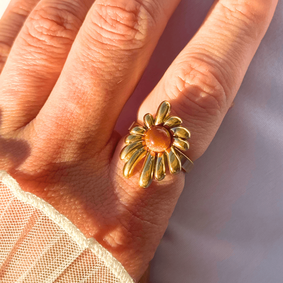 Gold flower-shaped ring on a person's finger with a soft background