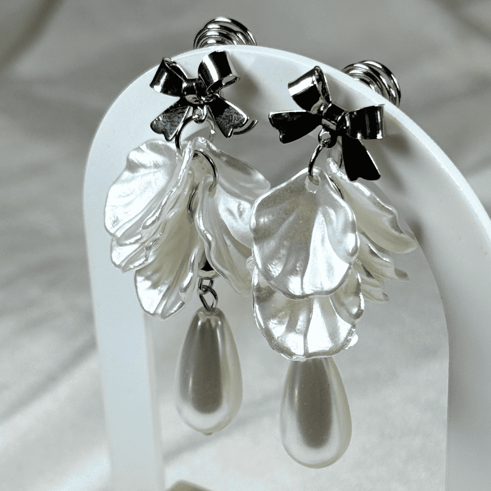 Silver earrings with leaf-like pendants and teardrop shapes on a white stand.