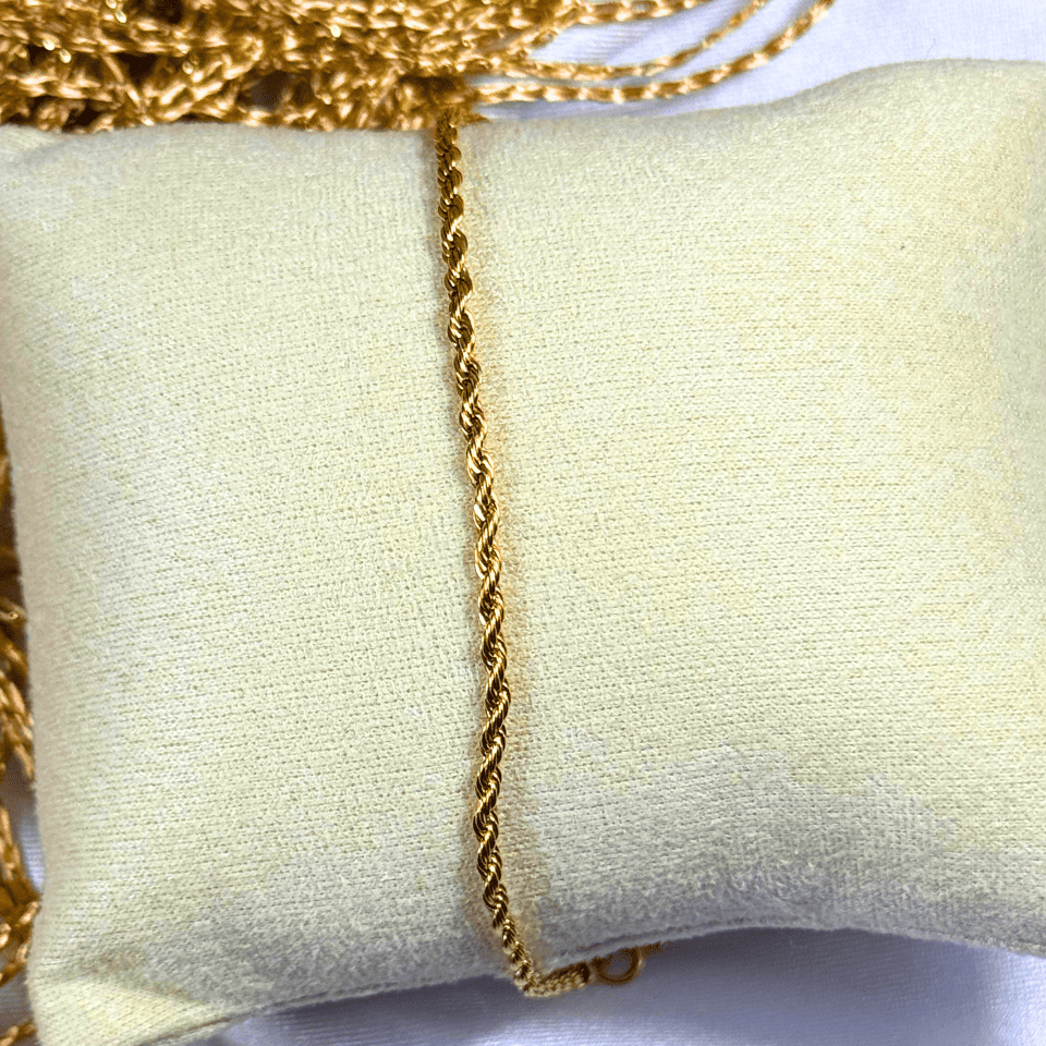 Gold chain necklace on a light beige cushion with a white background