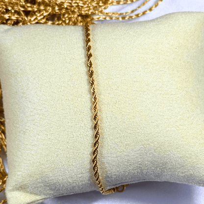 Gold chain necklace on a light beige cushion with a white background