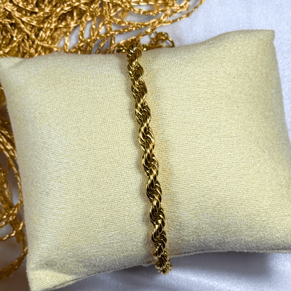 Gold rope chain necklace on a beige pillow with a white background