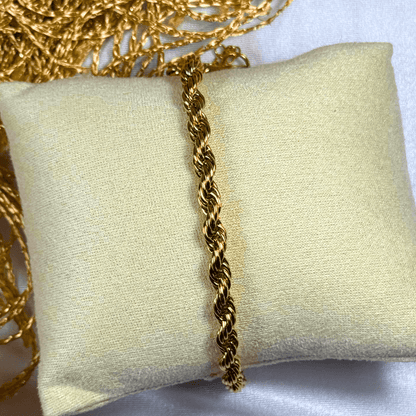 Gold rope chain necklace on a beige pillow with a white background