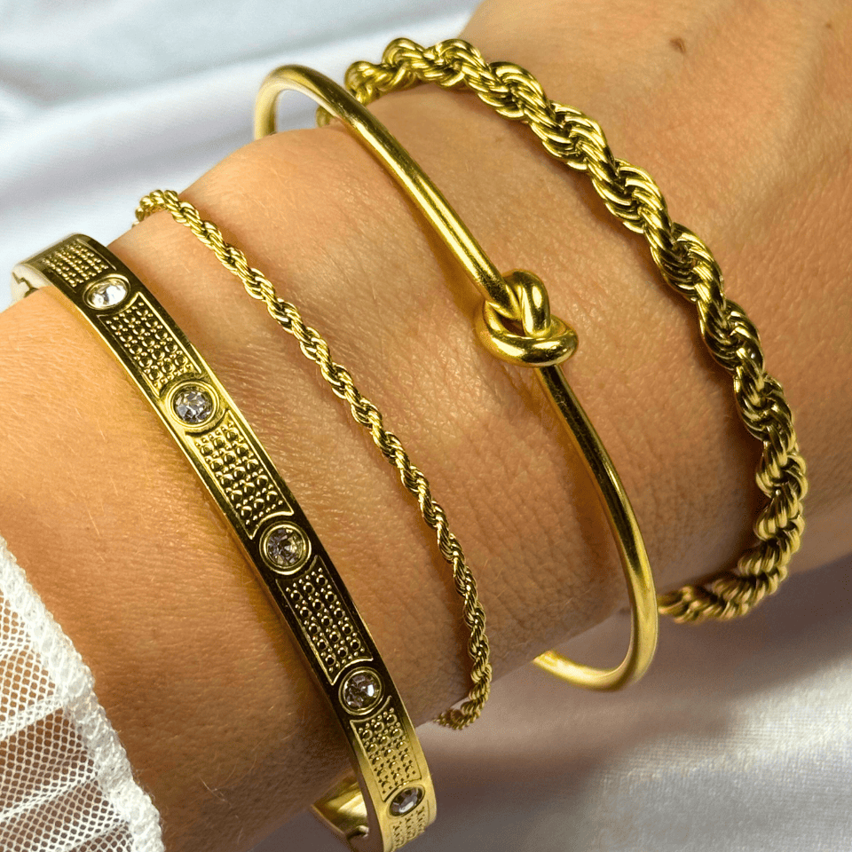 Gold bracelets on a wrist with a white lace fabric background