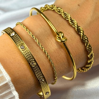 Gold bracelets on a wrist with a white lace fabric background